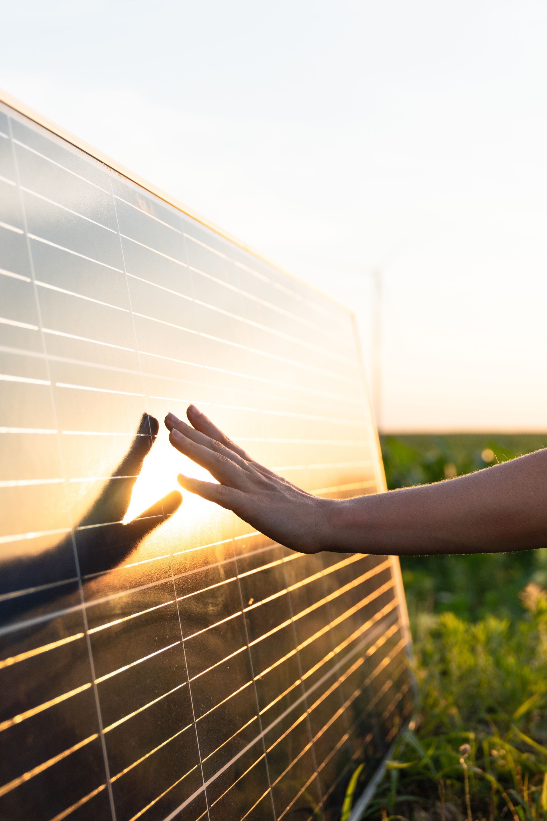 Close-up of a hand touching a solar panel at sunset.